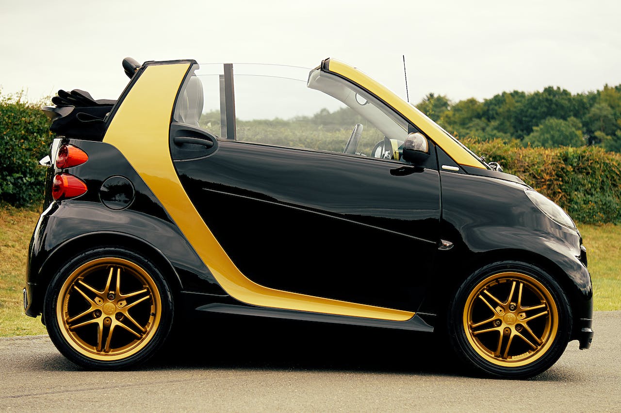 Automobil negru cu accente galbene, cu roți aurii și descoperit, parcat pe iarbă